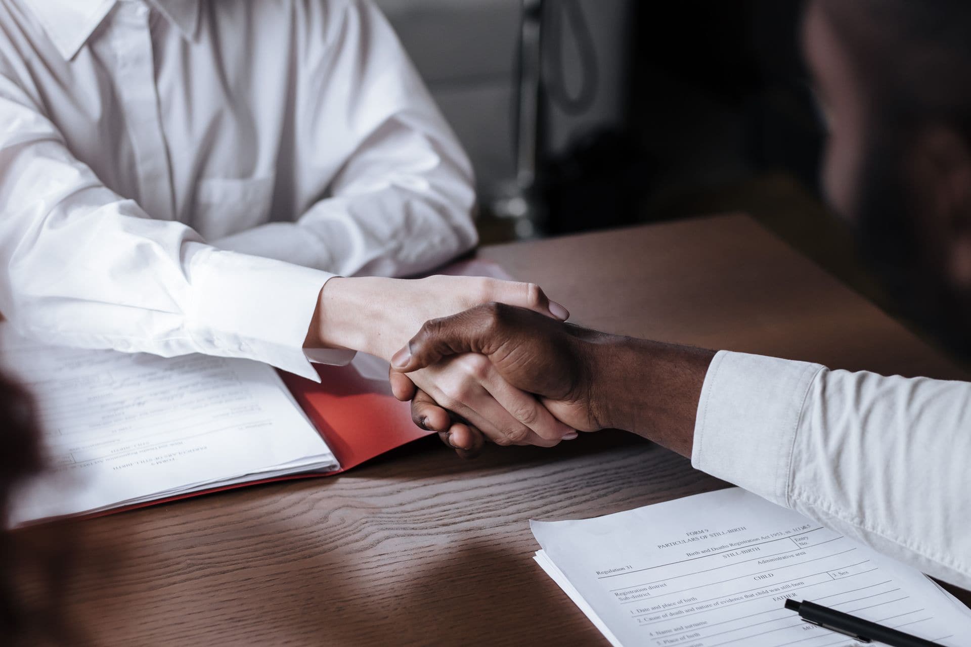 Two professionals shaking hands over documents at a desk